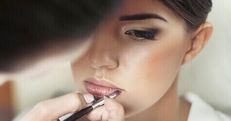 Makeup artist applies lipstick to a woman with a brush.