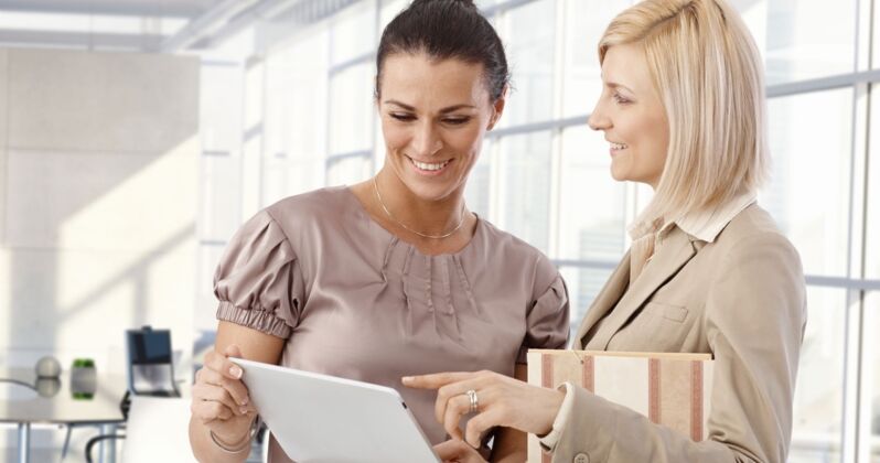 Zwei Frauen im Büro schauen gemeinsam auf ein Tablet und besprechen etwas.
